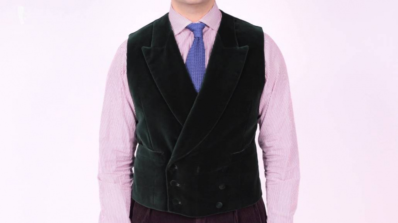 Raphael portant un gilet en velours noir à double boutonnage, une chemise à manches longues rose et une cravate en tricot bleu