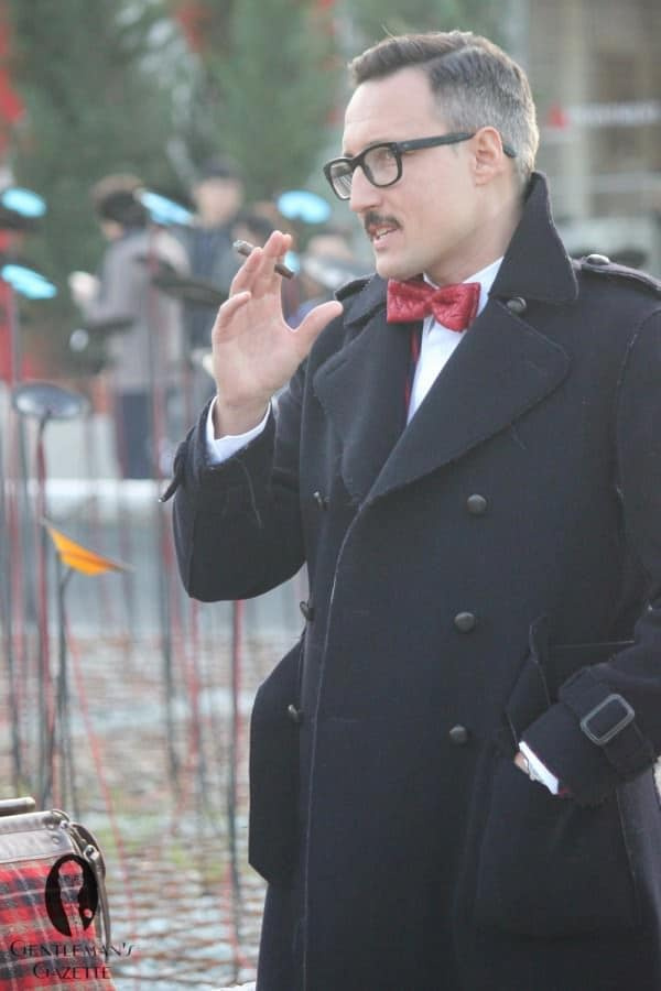 Фотографија мушкарца са цигаром са дуплим копчањем и излизаним ивицама упарен са црвеном кожном лептир машном