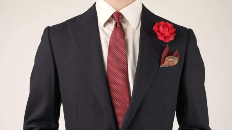 Laivastonsininen puku, jossa on silkkijacquard-valkoisia pilkkuja, silkkivillainen taskuneliö ja punainen camellia boutonniere.