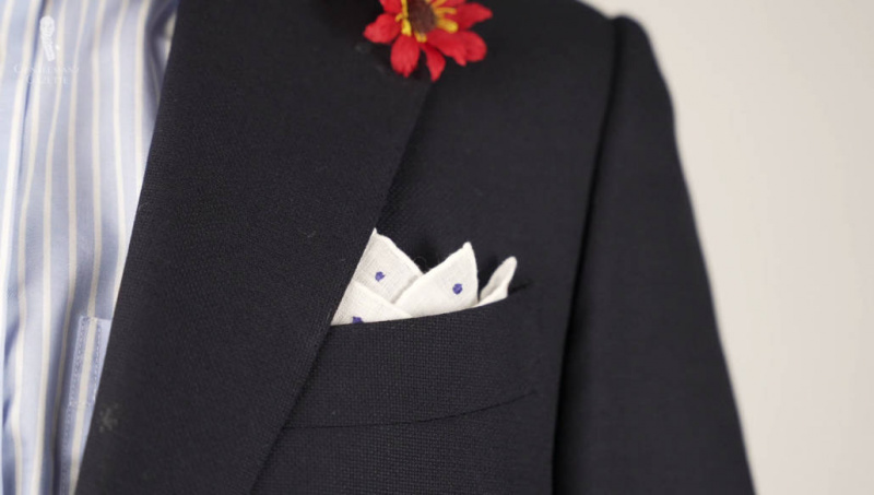 Laivastonsininen puku, jossa on sininen ja valkoinen paita, jossa on valkoinen taskuneliö, jossa on sinisiä pilkkuja ja punainen boutonniere.