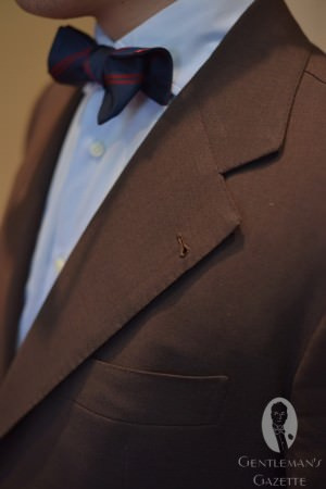 Jaqueta marrom com camisa azul clara e gravata borboleta azul vermelha listrada