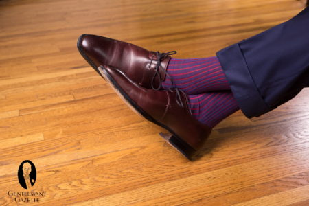 Une paire de chaussures Oxblood Derby avec un pantalon bleu marine et des chaussettes côtelées Shadow Stripe Navy Blue and Red Fil d