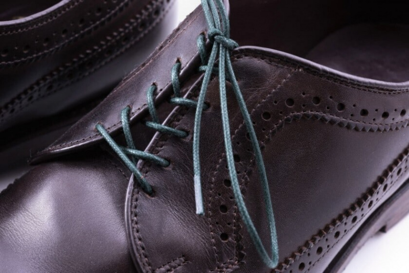 Cadarços verdes escuros usados ​​em um sapato de couro escuro