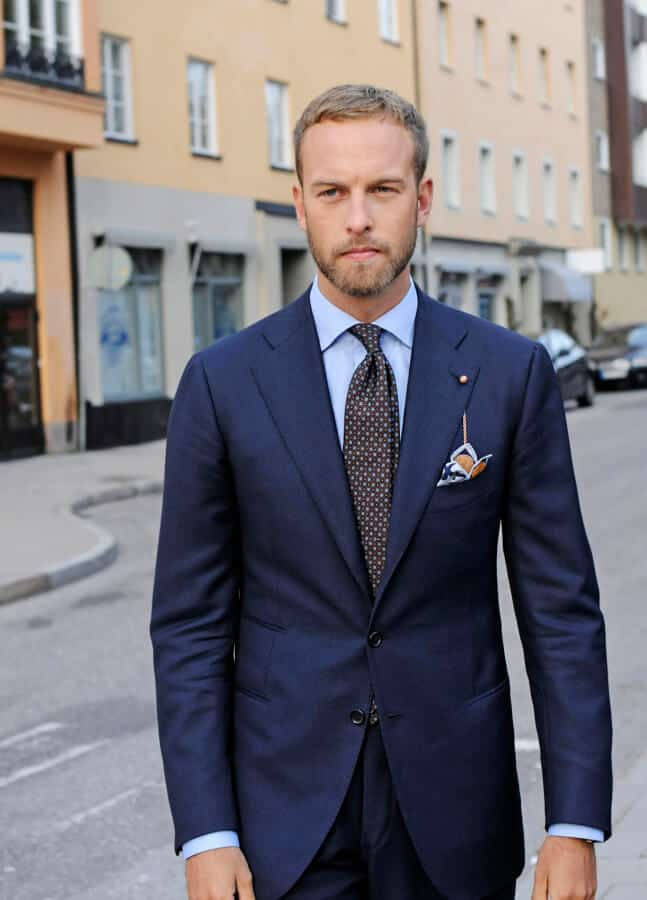 Andreas dans une palette de couleurs bleu-marron typique avec pochette de costume imprimée et chaîne de revers