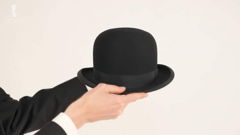 Preston mostrando a aba de um chapéu-coco preto com uma faixa preta.