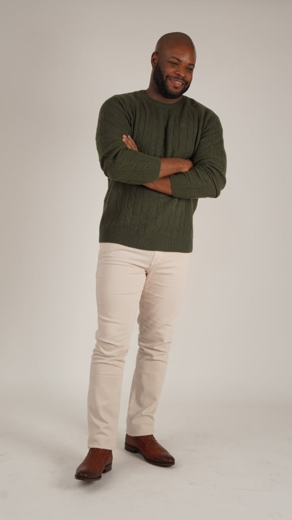 Kyle; aos 30 anos, vestindo suéter de tricô verde combinado com jeans de cor creme e bota de couro marrom.