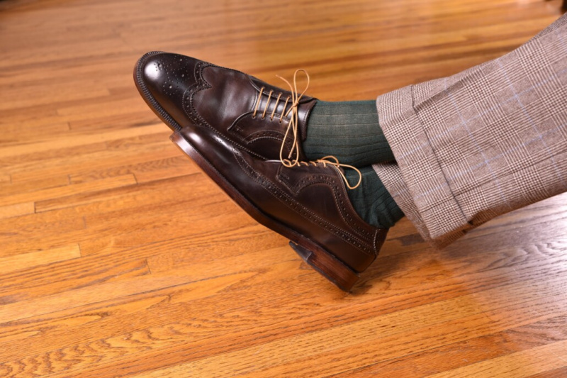 Tmavě hnědé kordované boty v kombinaci se zelenými ponožkami a kostkovanými kalhotami