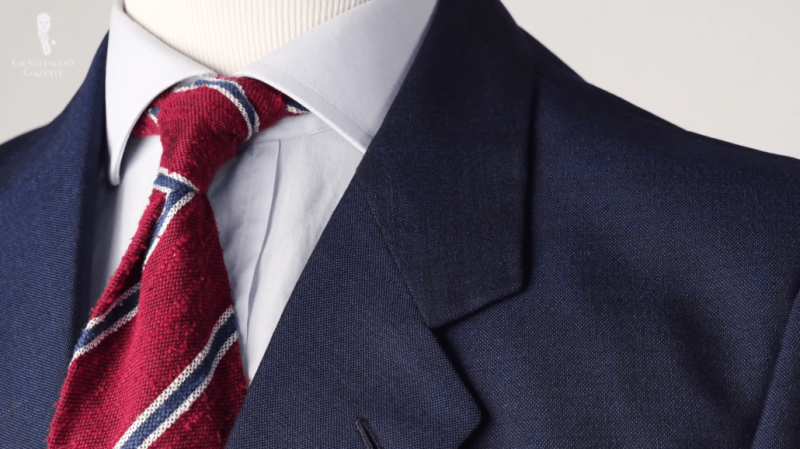 Une veste bleue, une chemise bleu pâle et une cravate rayée en shantung rouge, bleu et blanc