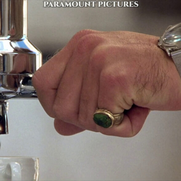 Detailní pohled na Dickieho malíček se zeleným kamenem a jeho 30metrové quartzové hodinky Swanson.