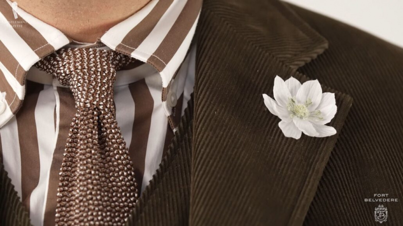 La cravate en tricot marron et beige complémentaire et la boutonnière fleur de lotus blanche et verte de près