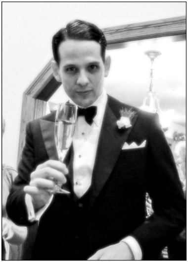Sven Raphael Schneider en smoking portant un toast au spectateur avec une flûte à champagne