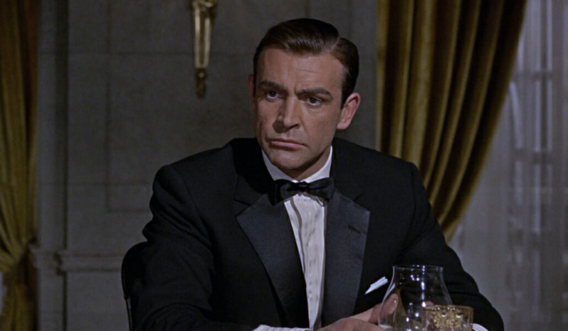 Sean Connery em smoking de lapela entalhada em 1964 - Goldfinger É um dos exemplos mais citados de legitimidade de lapela entalhada. No entanto, o contexto da cena sugere o contrário