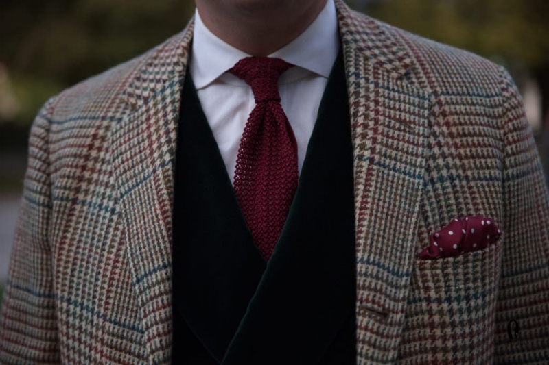 Zelená vesta s červenou pletenou kravatou a vínovým puntíkovaným kapesníkem s károvaným tvídem prince z Walesu