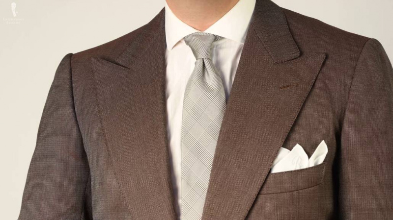 Hnědý vzorovaný oblek s šedou kravatou.