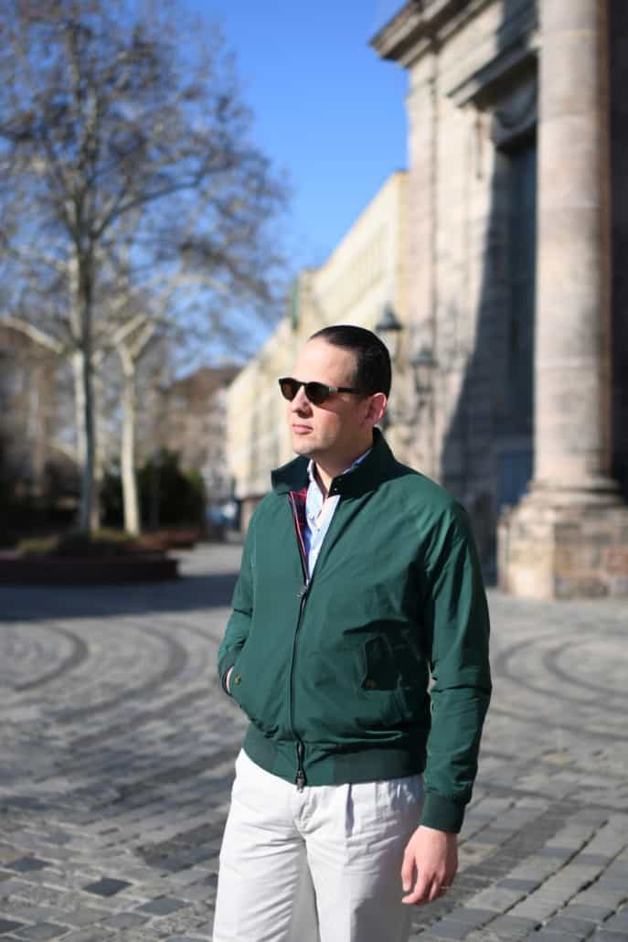 Raphael na sobě zelenou bundu G9 Harrington Jacket Baracuta, bílé chinos kalhoty a sluneční brýle.