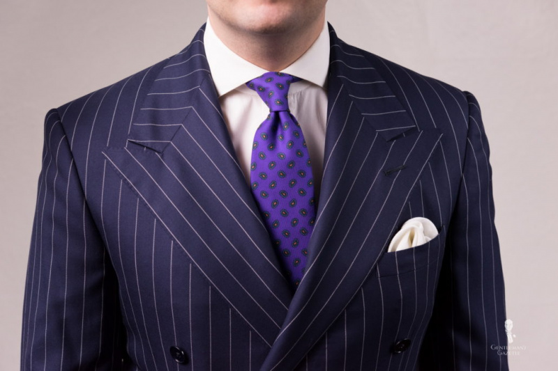 Costume à motifs bleu marine associé à une chemise de ville blanche, une cravate en soie Madder violette avec Paisley Fort Belvedere et une pochette de costume blanche