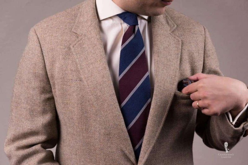 veste marron à chevrons associée à une cravate rayée grenadine rouge et bleu.