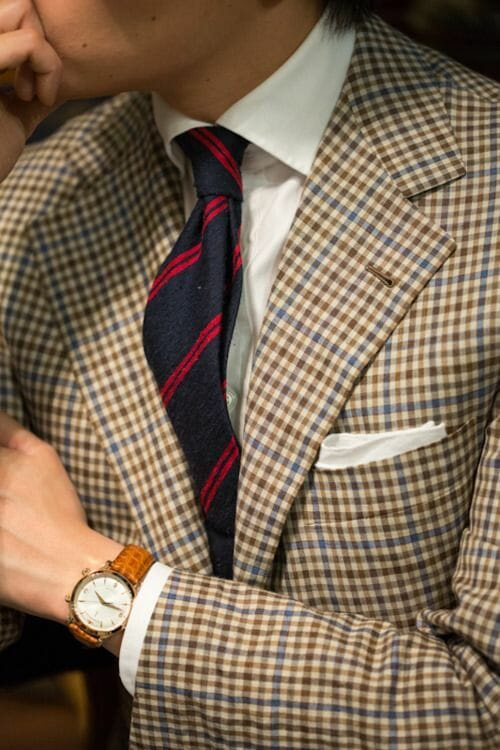 Uma jaqueta xadrez do clube de tiro, uma camisa branca lisa e lenço de bolso e uma gravata listrada azul e vermelha.