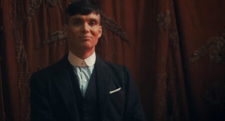 Peaky Blinders のキャラクターである Tommy Shelby の写真で、ネックウェアのない取り外し可能な襟とダーク スーツを着用しています。