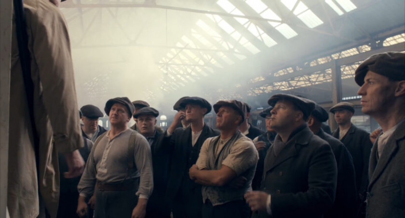 テレビ シリーズの Peaky Blinders のスクリーン ショットで、多くの労働者階級の男性が典型的な時代の服装をしている様子が示されています。
