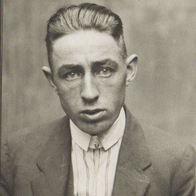 Црно-бела фотографија човека са крунисаном зализаном подшишаном косом.