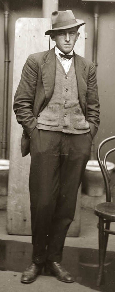 Černobílá fotografie muže v denním obleku ve vestě a motýlku.