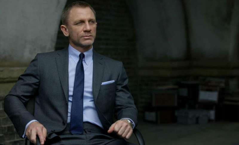 Daniel Craig dans le rôle de James Bond dans un costume gris moyen avec une cravate bleu moyen.