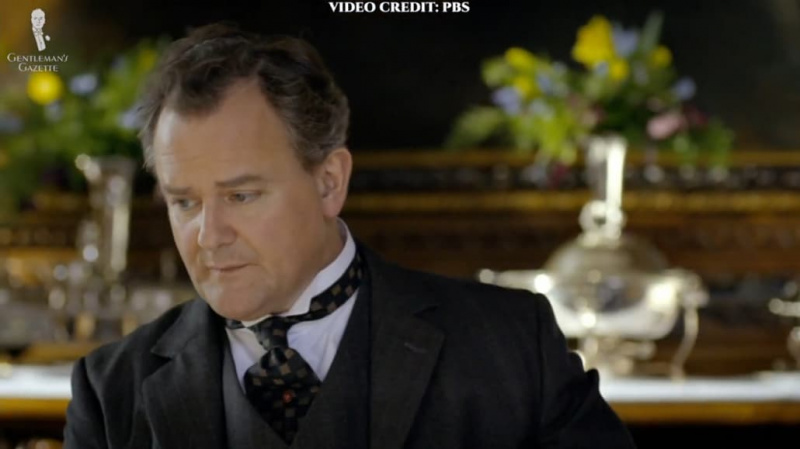 Lord Grantham na sobě černý oblek a kostkovaný nákrčník
