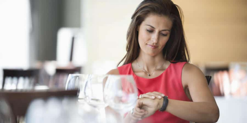 Moteris sėdi restorane ir žiūri į rankinį laikrodį