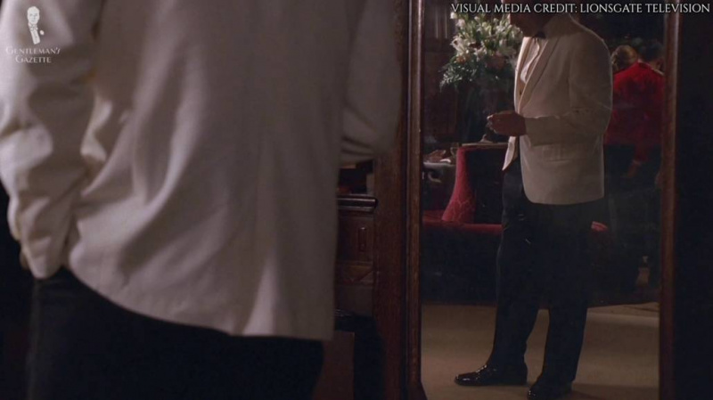 Un reflet dans le miroir montrant Don Draper portant un pantalon noir et des chaussures noires avec son smoking.
