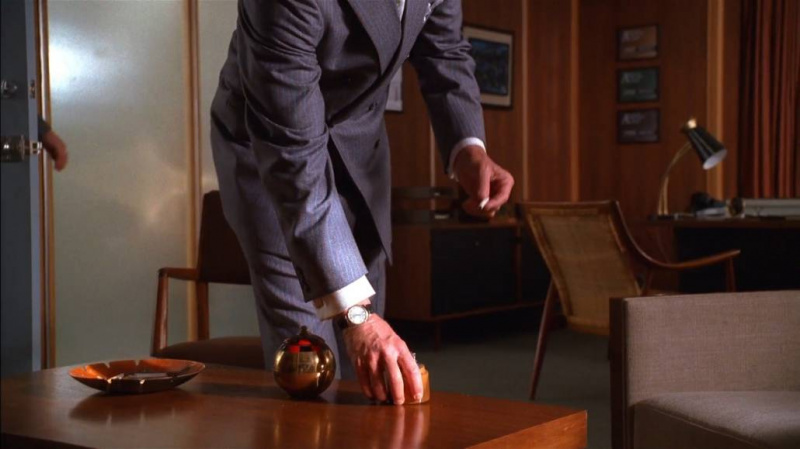 Don Draper ostentando um punho francês e abotoaduras de metal. Ele