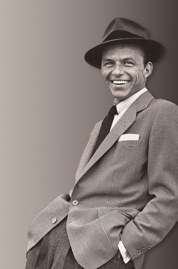Sinatra portant un chapeau signature, un manteau de sport, une cravate sombre et une épingle de col de sécurité