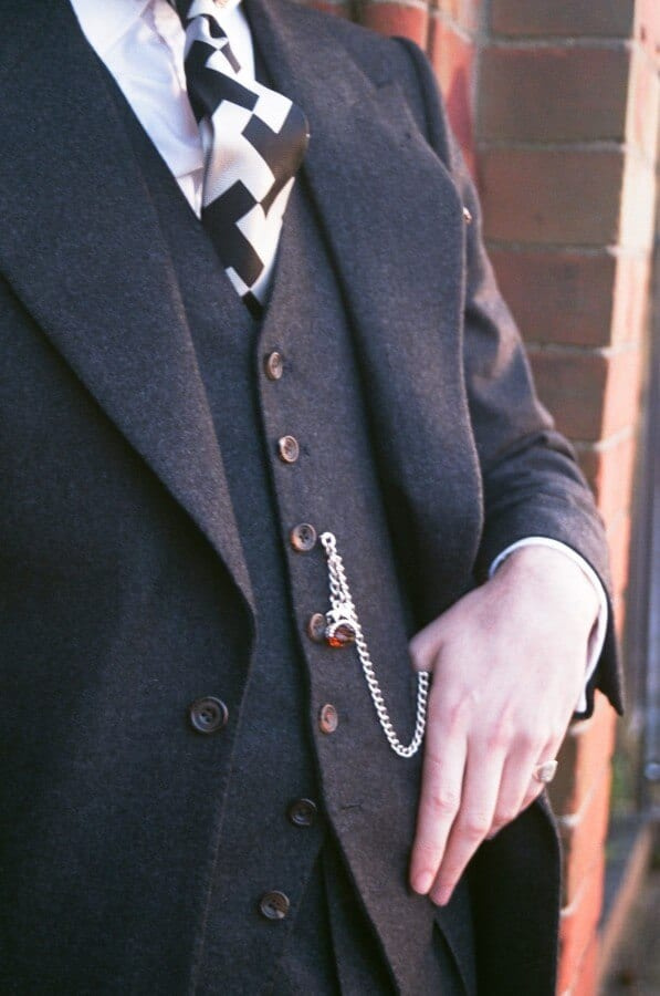 Observe que Aleks usa uma Albert Watch Chain com FOB e mantém os dois botões inferiores de sua jaqueta desabotoados