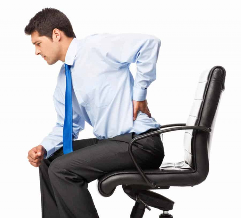 Mladý podnikatel s bolestí zad sedí v kancelářské židli.