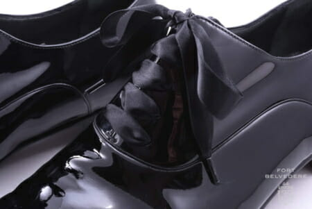 Cadarços de noite de cetim preto em um par de sapatos de couro envernizado