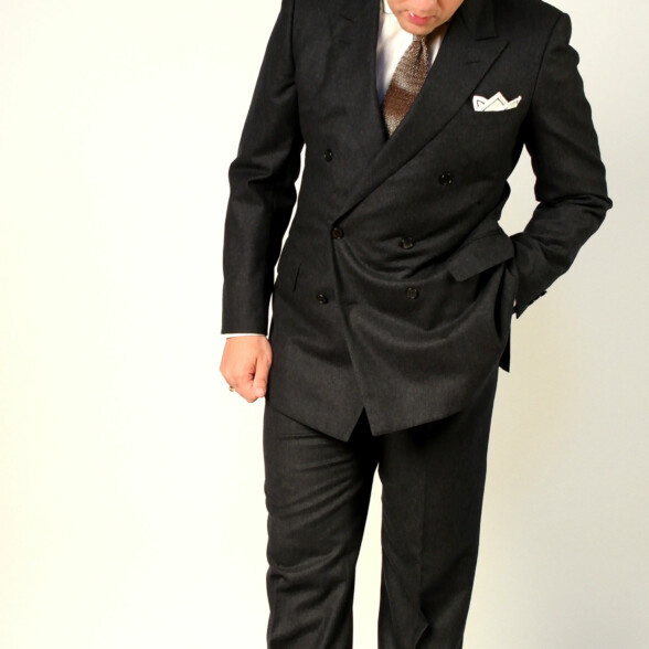 Sven Raphael Schneider nosí klasický šedý flanelový oblek s pletenou kravatou a tmavě hnědé semišové Chelsea boty
