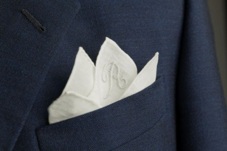 Een wit pochet in een kostuumzak, geborduurd met een initiaal