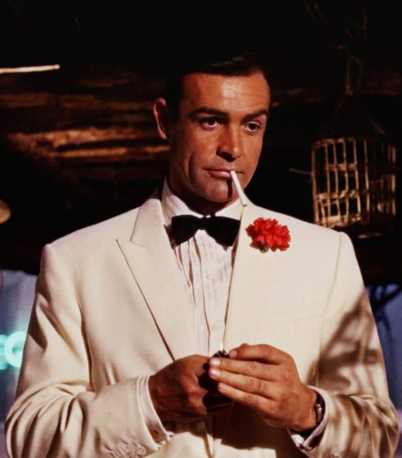 Шон Конери у улози Џејмса Бонда у белом сакоу за вечеру са дугметом од црвеног каранфила