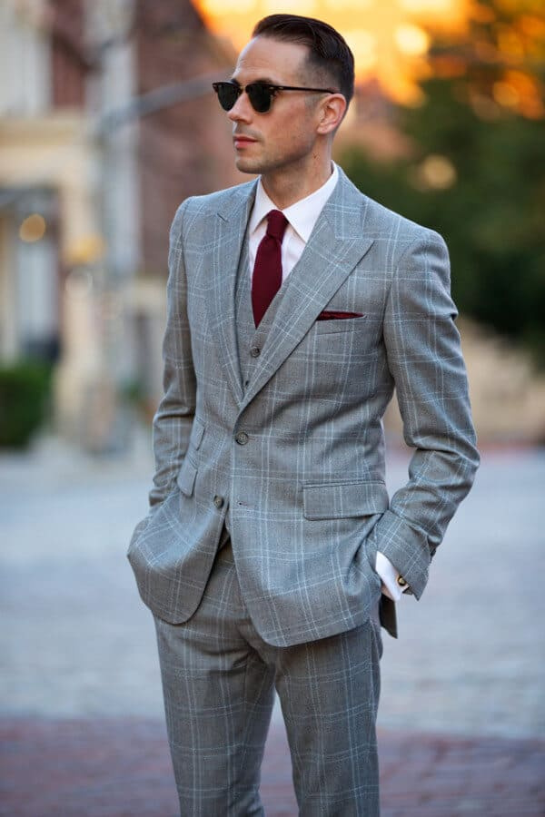 Brian portant un costume trois pièces à carreaux gris avec une cravate et une pochette bordeaux - He Spoke Style