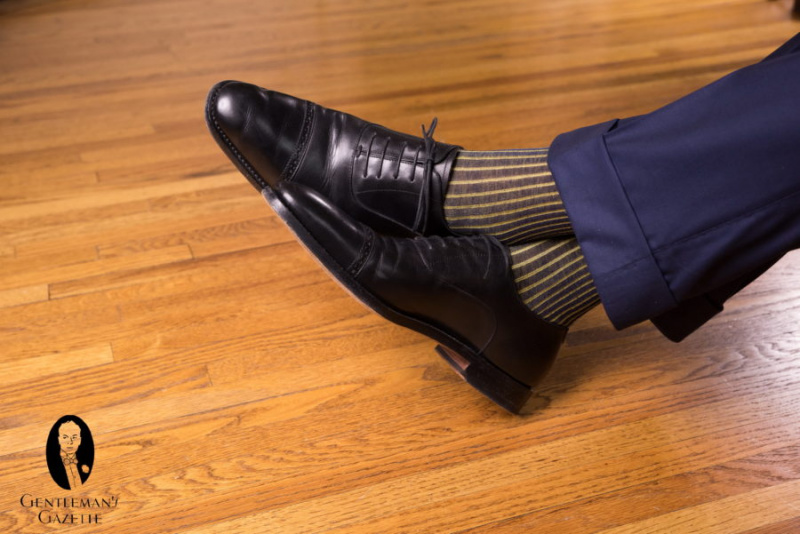 Црне оксфордице са морнарским панталонама и тамноплавим и жутим пругастим чарапама у сенци